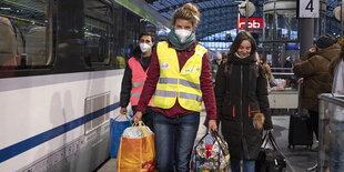 Personen in leuchtenden Warnwesten tragen voll bepackte Taschen auf dem Bahnsteig