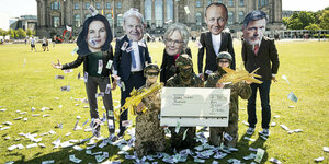 Aktivisten stehen vor dem Bundestag mit Masken von Baerbock, Scholz, Lambrecht, Merz und Habeck werfen mit Geld um sich