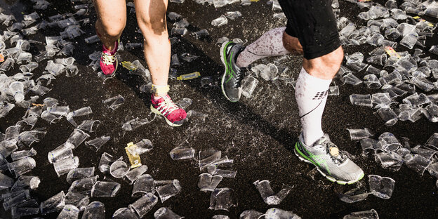 Maratohnläufer:innen laufen durch Plastikbecher.