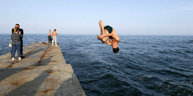 Eine Person spring von einer Brücke ins Wasser.
