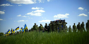 Soldaten tragen einen Sarg übers Feld, gefolgt von Menschen mit ukrainischen Flaggen