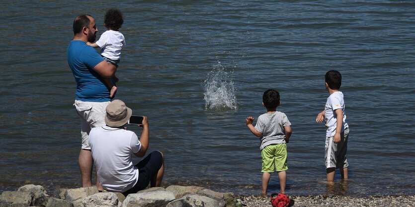 Zwei Väter und am Wasser spielende Kinder