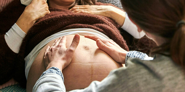 Eine Hebamme tastet den Bauch einer schwangeren Frau ab