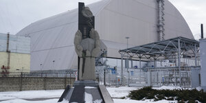 Halbrunde Abdeckung des beschädigten Kraftwerks in Tschernobyl, davor ein Denkmal
