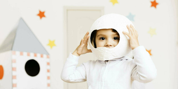 Ein kleines Mädchem mit Papphelm auf dem Kopf spielt Astronautin