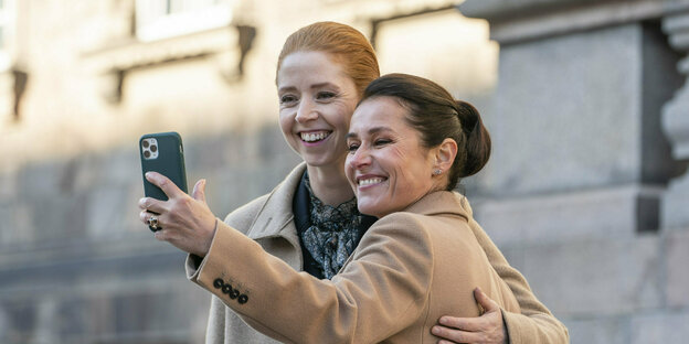 Zwei Frauen aus der Politserie "Borgen" schauen auf ein Smartphone.