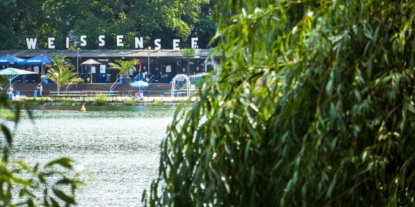 Eine Wasserfläche, dahinter ein Strandbadgebäude mit der Aufschrift "Weissensee".