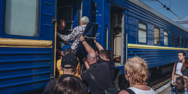 Ein Mann mit eingeschränkter Mobilität wird in einen Zug gehoben.