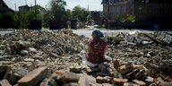 Eine Frau sitzt auf den Trümmern eines Hauses.
