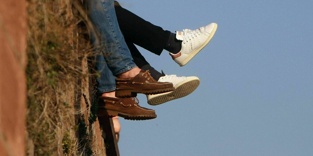 Personen genießen die Sonnenstrahlen auf einer Mauer und lassen die Beine baumeln