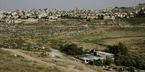 Eine israelische Siedlung auf weitem Feld, davor ein kleines palästinensisches Haus.