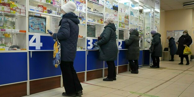 Vier ältere Frauen stehen an den Schaltern einer Apotheke