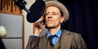 Ein Mann im karierten Anzug und mit Hut auf spricht in ein Aufnahmemikrofon