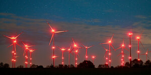 Die roten Positionslichter an windenergieanlagen erhellen den Nachthimmel und die Landschaft.