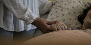 Eine Pflegerin hält einer Seniorin die Hand