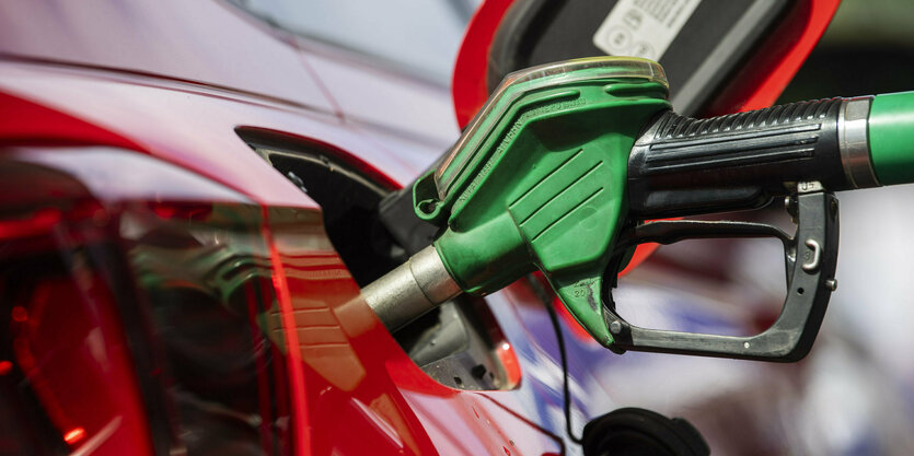 Ein Auto wird an einer Tankstelle betankt. Man sieht den Zapfhahn, wie er das rote Auto befüllt.