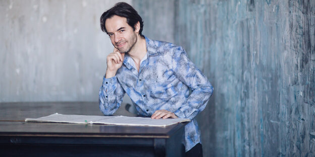 Lakonisch und zugleich mit konstant hoher Energie: der ukrainische Pianist Vadim Neselovskyi, hier sitzt er in einem blauen Hemd am Tisch.