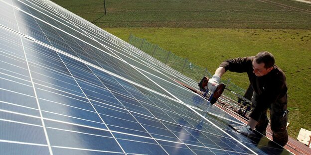 Ein Mann binrt ein Solarpanel an einem Dach an