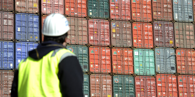 Ein Mitarbeiter steht vor einer Wand aus gestapelten Containern