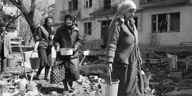 Eine Frau trägt Wassereimer durch eine kriegszerstörte Stadt