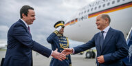 Scholz reicht Albin Kurti die Hand, im Hintergrund ein Flugzeug und ein Mann in Uniform