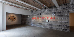 Innenansicht auf Mosaik vieler kleinerer S/W-Fotos von Yalter die überschrieben sind mit roter Schrift: Exile is a hard Job
