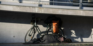 Mann schläft unter einer Brücke in Berlin, neben sich ein Fahrrad