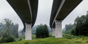 Zwei Autobahn-Brücken, die Kamera ist unter ihnen positioniert und schaut nach oben, drumherum ist viel Grün