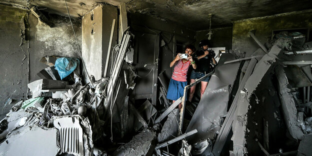 Zwei Menschen fotografieren in einer von Artilleriebeschuss völlig zerstörten Wohnung