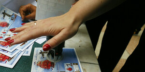 Eine Hand stempelt Briefmkarkenblöcke, auf denen man ein Schiff mit roten Segeln sieht