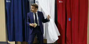 Emmanuel Macron trägt Anzug und verlässt die Wahlkabine in den Farben Blau, Weiß, Rot