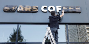 Ein Mann steht auf einer Leiter und entfernt die Folie von "Stars Coffee" an der Fassade