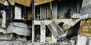 Ein Haus mit weggesprengter Fassade. Innen Trümmer, Bäder, ein Bett, eine heruntergestürzte Heizung