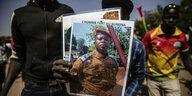 Menschen auf der Straße halten ein Bild von Oberstleutnant Paul-Henri Sandaogo Damiba in Militärkleidung in die Kamera
