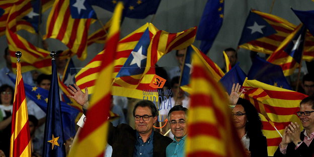 Zwei Männer lächeln und winken während sie von wehenden katalonischen Flaggen umgeben sind