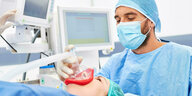 Ein Mann hält in einem Operationssaal einer Person eine Narkosemaske auf den Mund