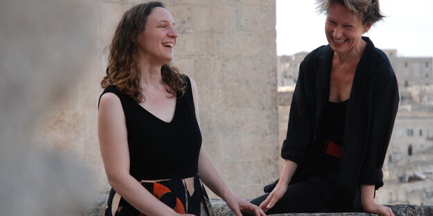 Die Musikerinnen Silvia Tarozzi und Deborah Walker lehnen amn einem Mauervorsprung und lachen