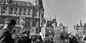 Ein altes Foto von 1937 zeigt eine Menschenmenge auf einem Platz in Barcelona, in ihrer Mitte sieht man eine Karikatur von Diktator Franco
