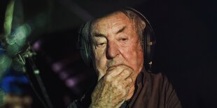 Nick Mason sitzt mit Kopfhörern hinter seinem Schlagzeug, Licht fällt ihm ins Gesicht, er hat die Hand ans Kinn gelegt