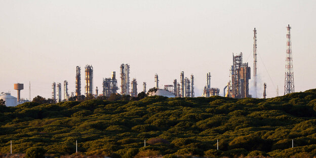 Ein sonnenbeschienener Hügel mit Anlagen einer Raffinerie im Hintergrund