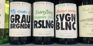 Mehrere Weinflaschen, auf den drei im Bild steht "Fifty shades of GRAUBRGNDR“, „Everything happens for a RSLNG“ und „Always sunny SVGNBLNC“