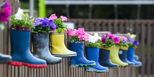 Kindergummistiefel mit Blumen hängen an Gartenzaun