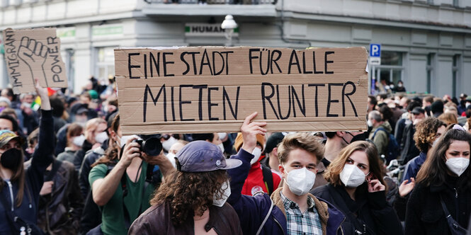 Menschen stehen in einer Menge mit einem Plakat, auf dem niedrigere Mieten gefordert werden