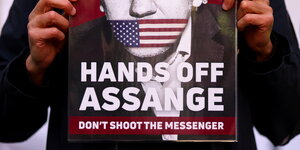 Ein Mensch hält ein Plakat, auf dem "Hands off Assange" steht hoch
