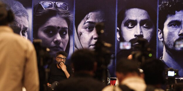 Der Filmemacher Vivek Agnihotri sitzt vor großen Szenenfotos aus ?The Kashmir Files?, im Vordergrund Journalisten von hinten.