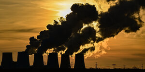 Kühltürme eines Kohlekraftwerks geben Dampf ab, im Hintergrund ein Sonnenuntergang.