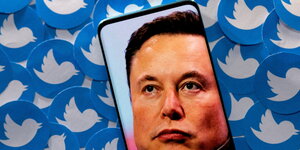 Elon Musk auf dem Display eines Smartphones, im Hintergrund lauter Twitter-Logos