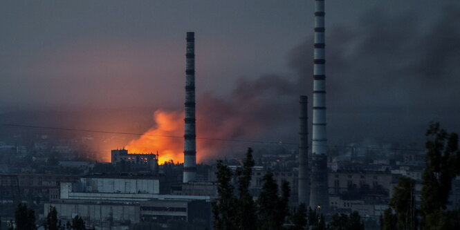 Chemiewerk mit zwei großen Schornsteinen und einem Feuer und Rauch im Hintergrund.