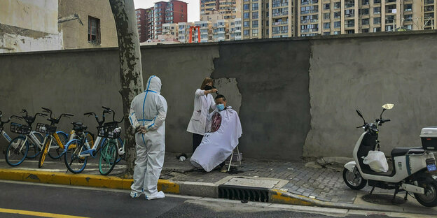 In Schanghai bekommt ein Mann auf der Straße unter Aufsicht die Haare geschnitten