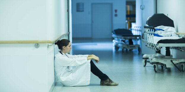 Eine Ärztin sitzt erschöpft am Boden auf dem Flur eines Krankenhauses